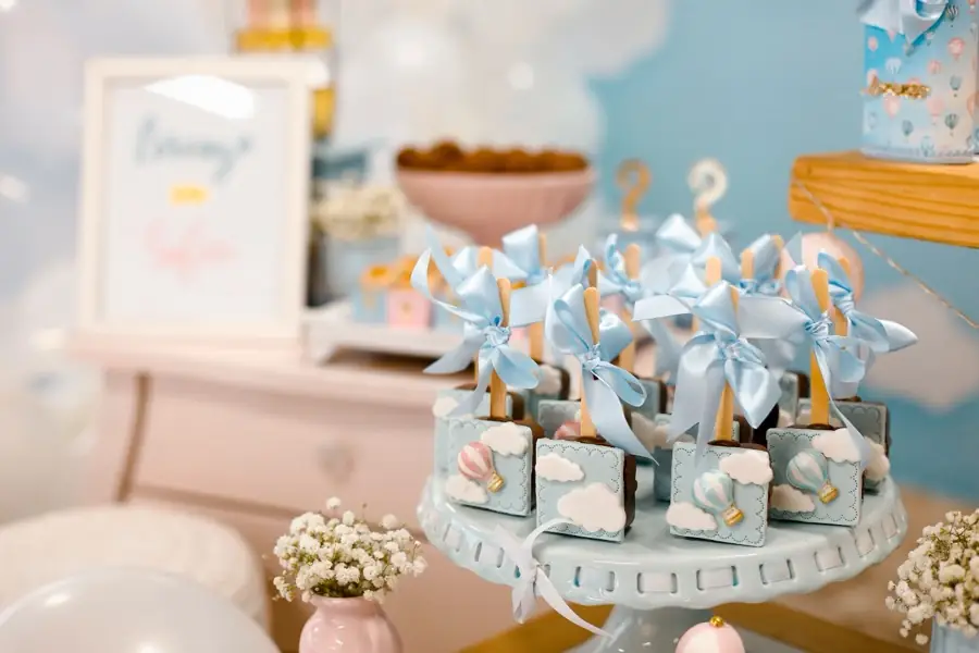 Table de baby shower aux tons pastel : boîtes cadeaux bleu ciel nouées de rubans sur un présentoir, fleurs blanches