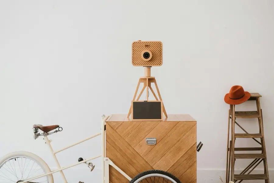 Cabine photobooth artisanale en bois clair surmontée d'un appareil photo décoratif, dans une pièce lumineuse
